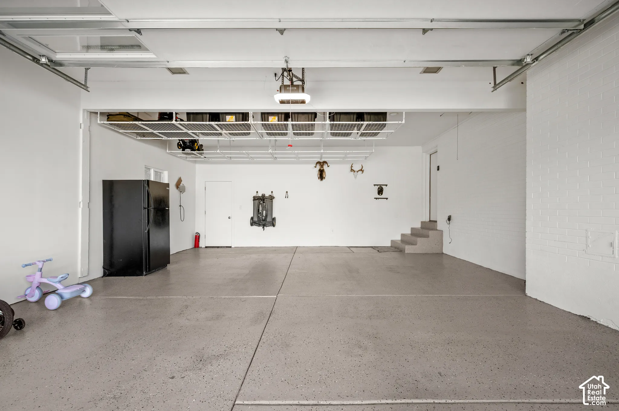 Spacious garage with light grey epoxy flooring, overhead storage racks, and white painted walls