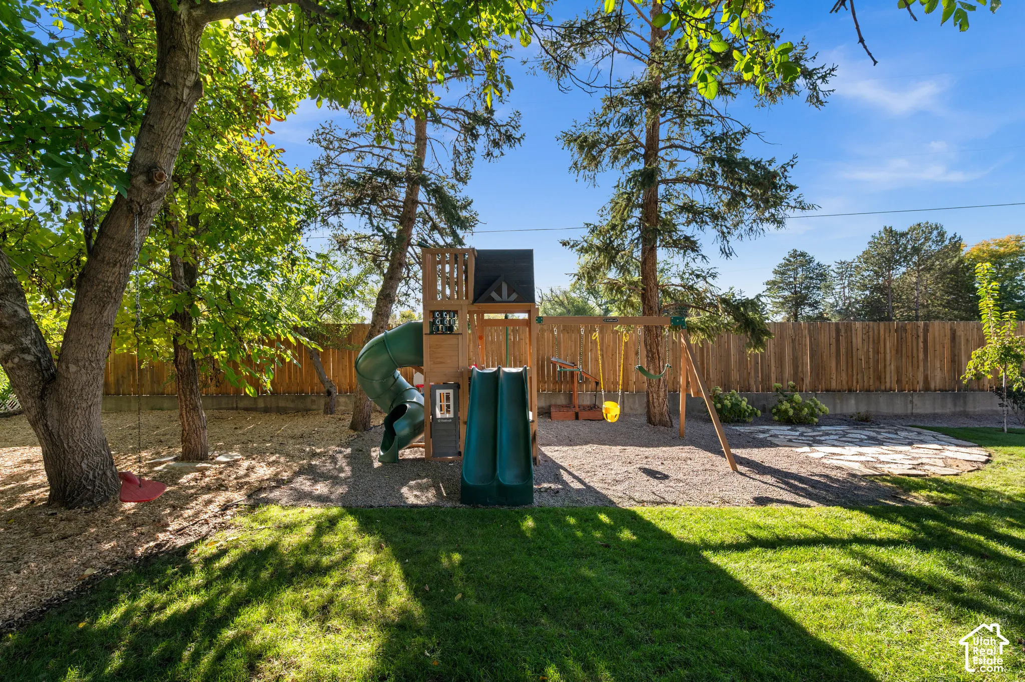 Expansive backyard featuring a manicured lawn, a wooden playset with multiple slides, and a privacy fence