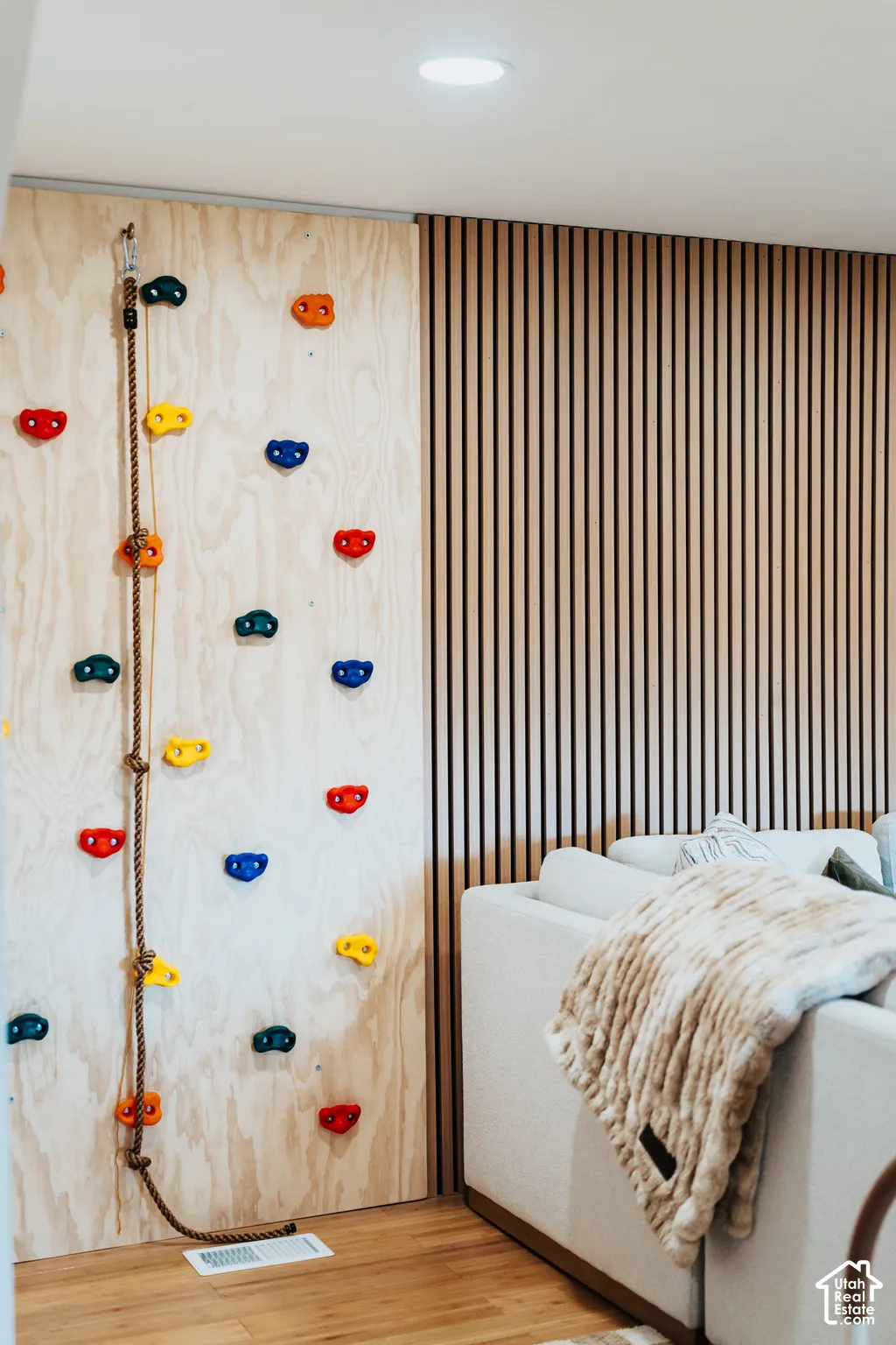 Custom-built indoor climbing wall with a climbing rope and multi-colored grips, set against an accent wall featuring vertical wood slat paneling