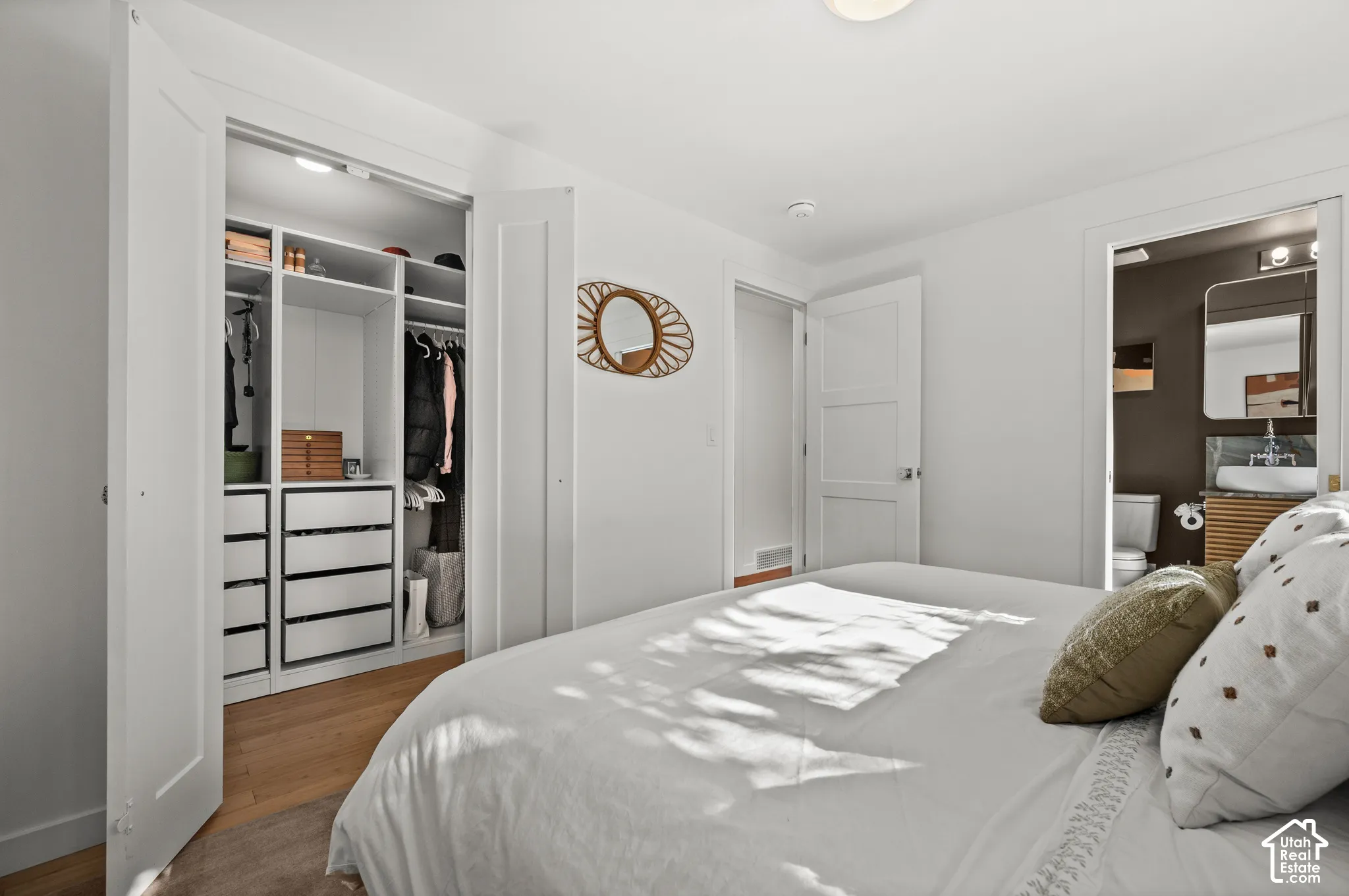 Built-in closet system with shelving and drawers, wood-finish flooring, white doors, and an attached bath with a vessel sink