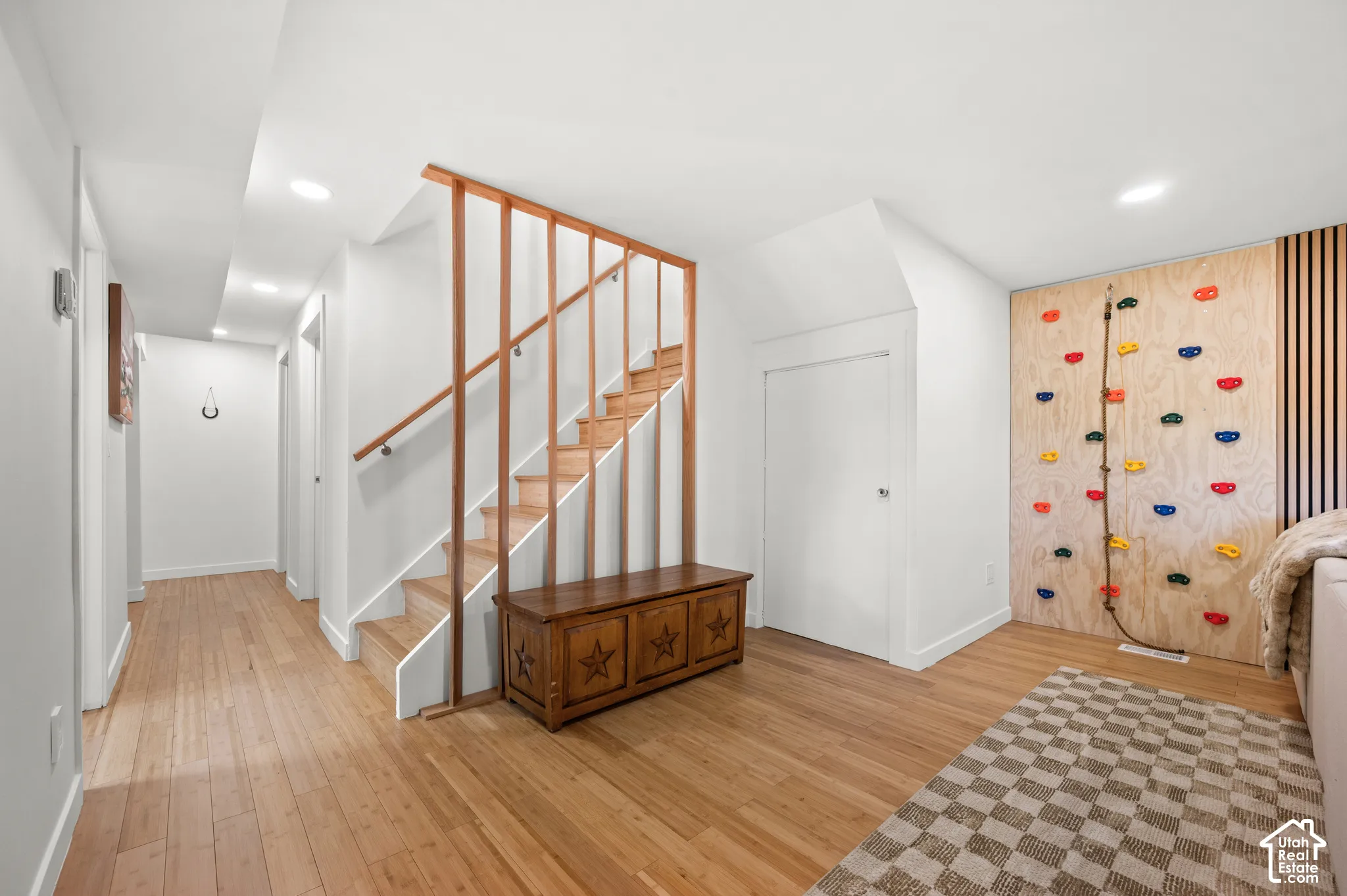 Wood-finish flooring throughout, light wood staircase with open railing, recessed lighting, and a built-in climbing wall