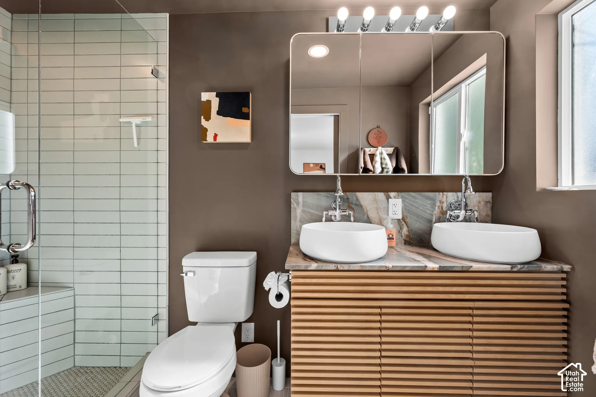 Dual vessel sinks set on a stone countertop with a slatted wood-finish vanity