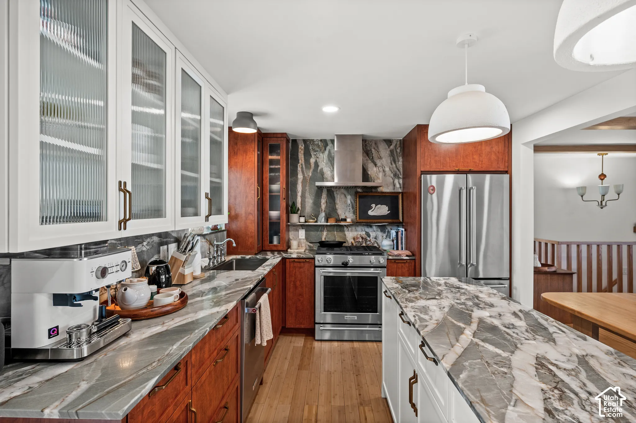 Kitchen featuring wood-finish flooring, white upper cabinetry with reeded glass doors, dark wood lower cabinetry, a stone-patterned backsplash, and a large central island with a stone countertop