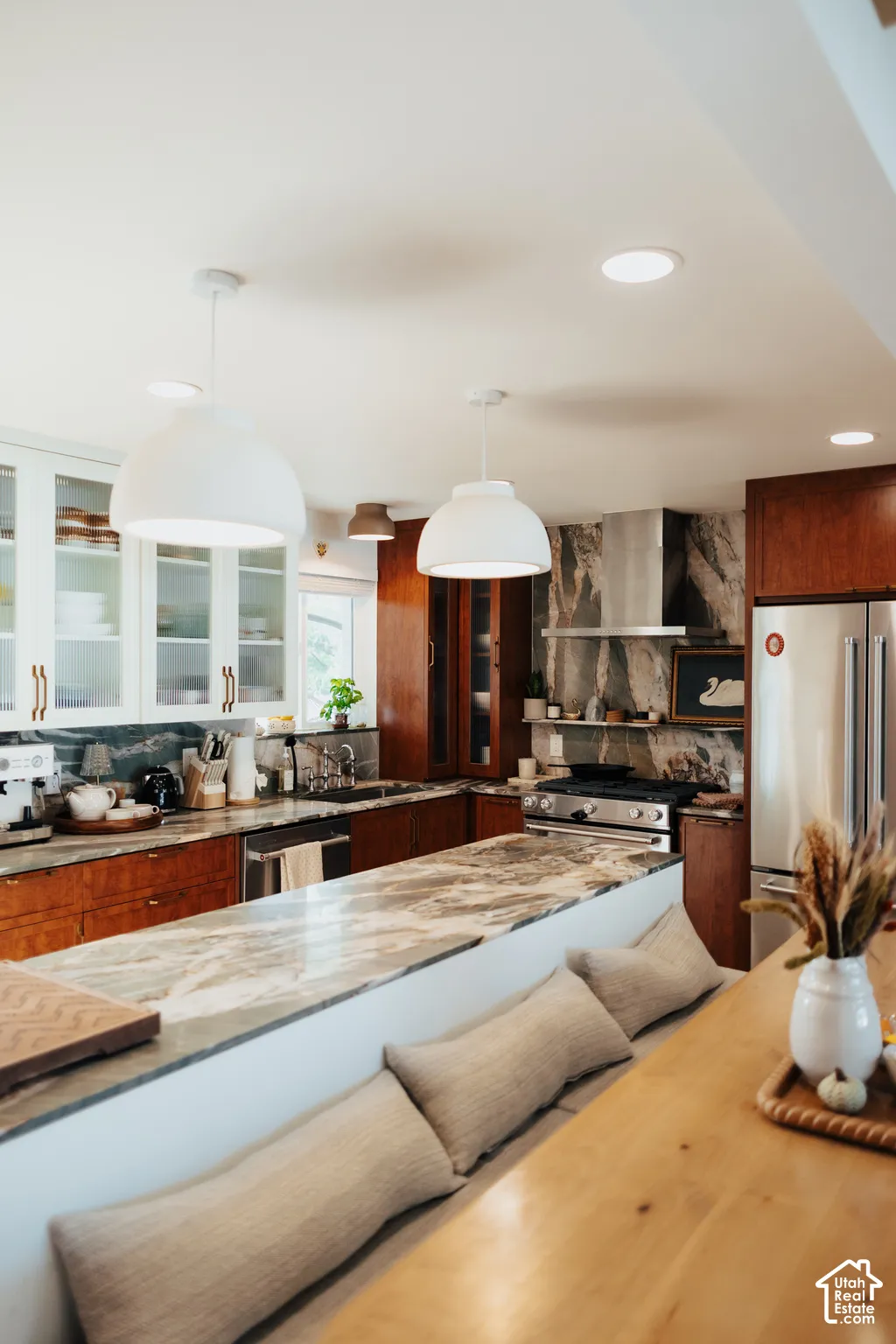 Kitchen featuring stone countertops, natural wood-finish cabinetry, white glass-front upper cabinets, stainless steel professional-style range hood, and dual oversized dome pendant lighting