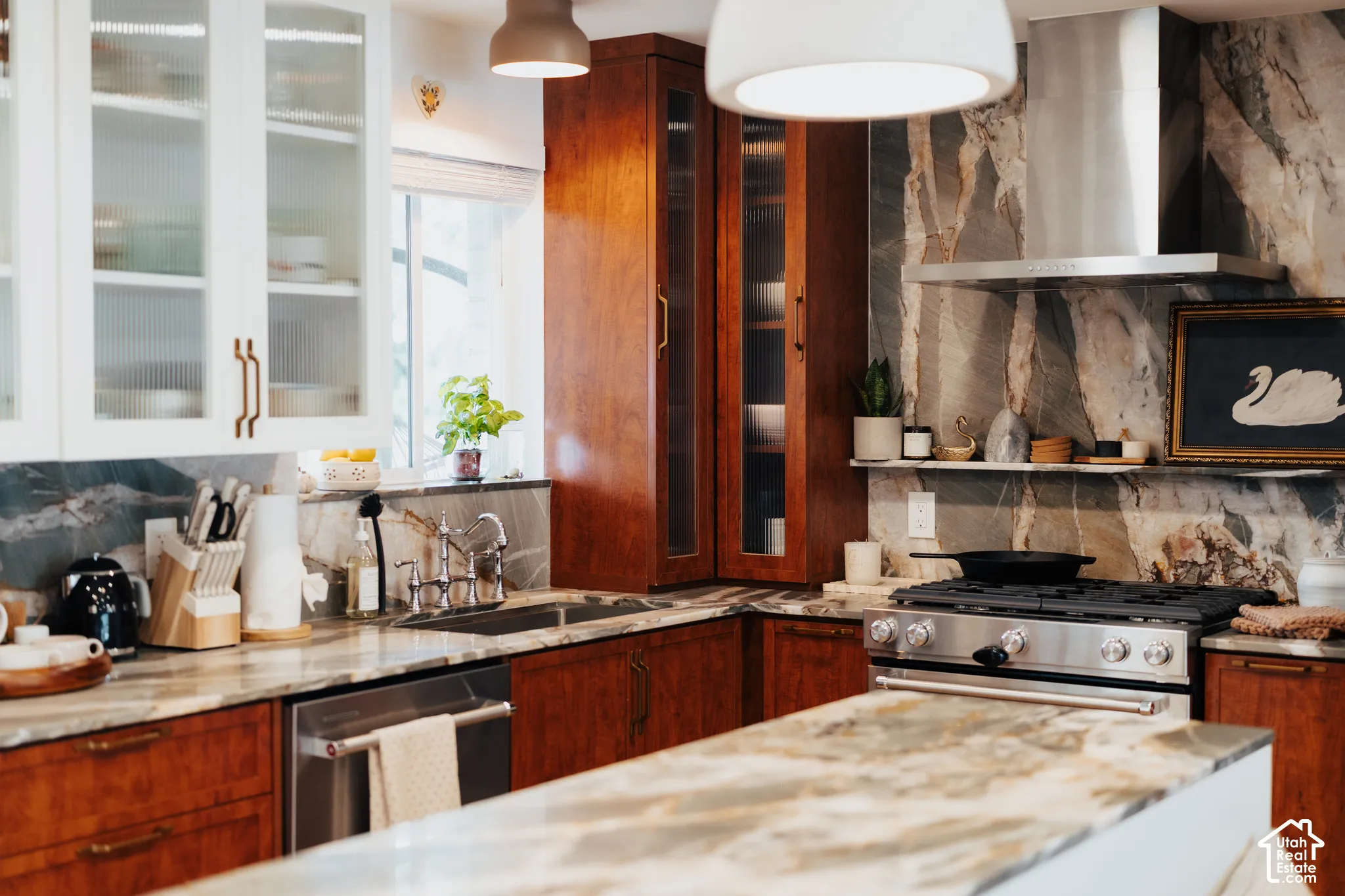 Kitchen featuring custom natural wood cabinetry, stone slab backsplash, quartz countertops, stainless steel gas range, and glass-paneled upper cabinets