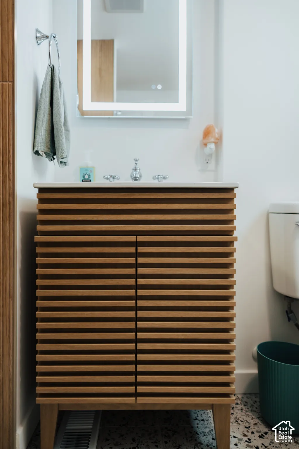 Custom vanity featuring horizontal wood-slat detailing, solid surface countertop, integrated LED-backlit mirror, and chrome widespread faucet
