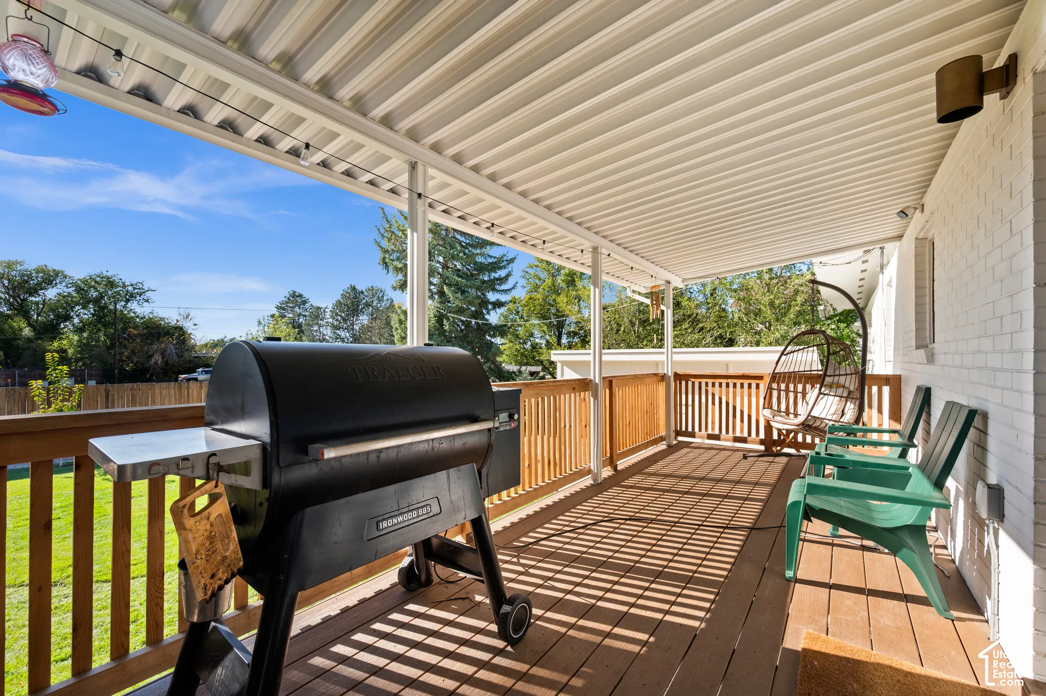 Covered outdoor deck with a white corrugated ceiling, wood-finish flooring, and white brick exterior