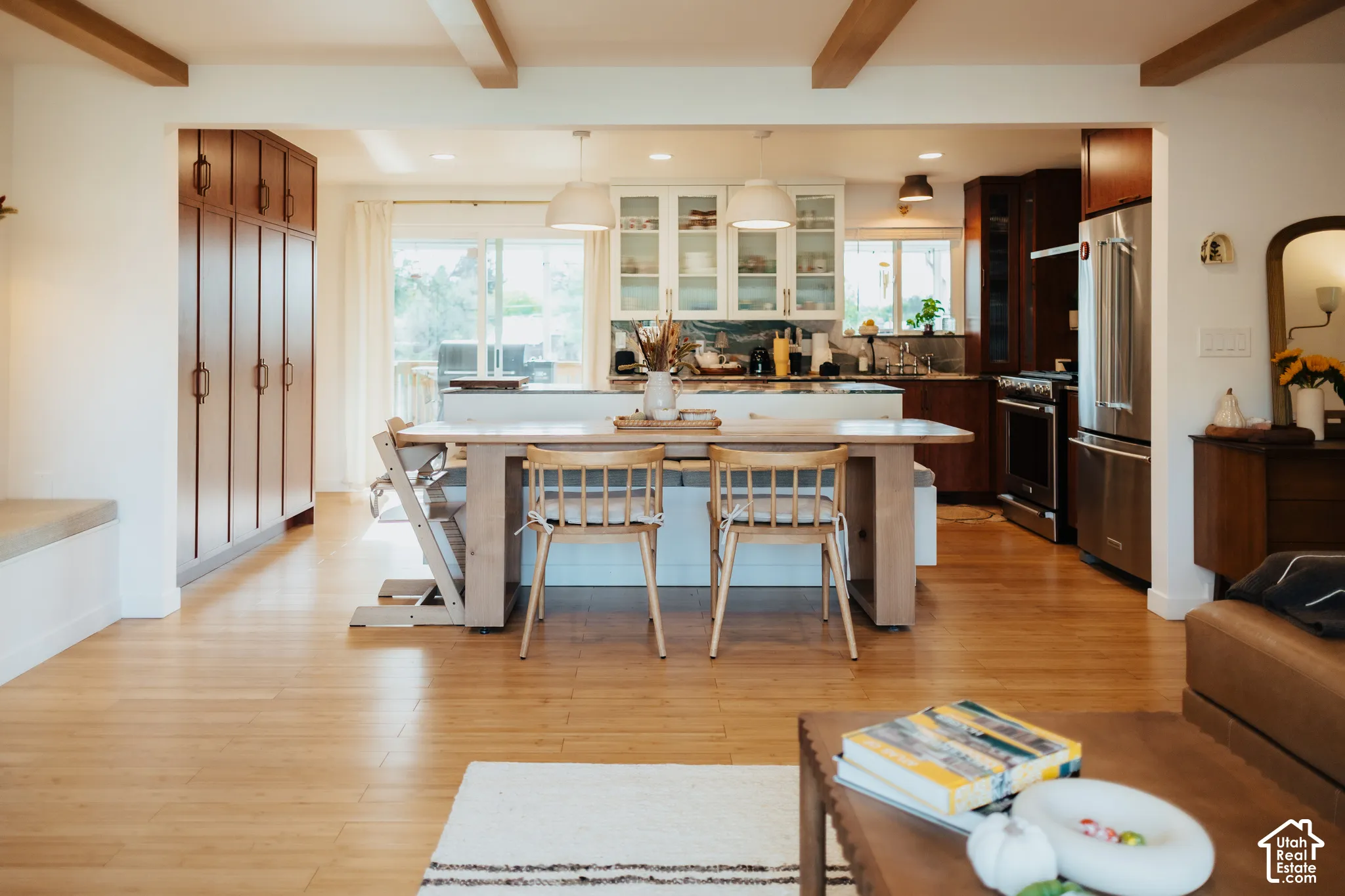 Kitchen featuring wood-finish flooring, exposed ceiling beams, full-height cabinetry, stainless steel appliances, and glass-front upper cabinets