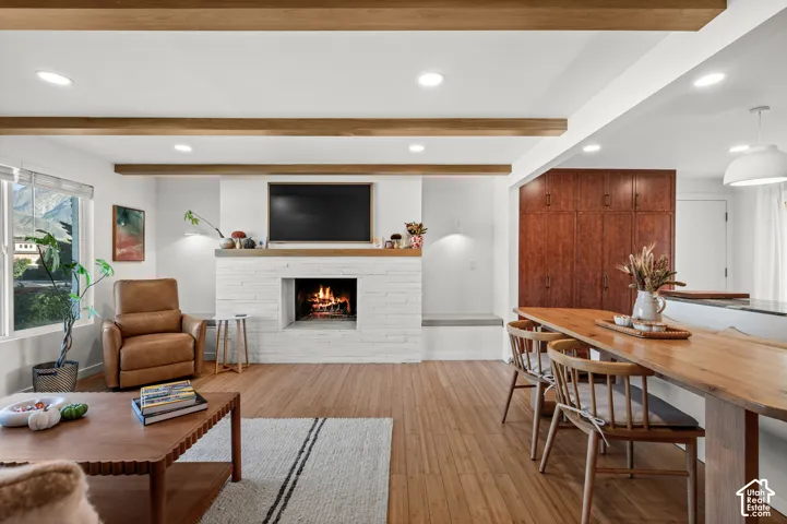 Exposed ceiling beams, wood-finish flooring, white brick fireplace with mantel, built-in wooden cabinetry, and pendant lighting