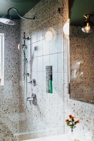 Shower enclosure featuring speckled tile surround, chrome multi-function shower system, built-in recessed storage niche, and a flush-mount brass globe light fixture