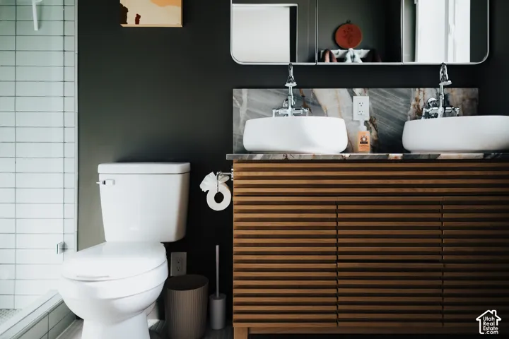 Slatted wood vanity featuring dual vessel sinks, stone backsplash, and wall-mounted faucets, accented by a rectangular mirror