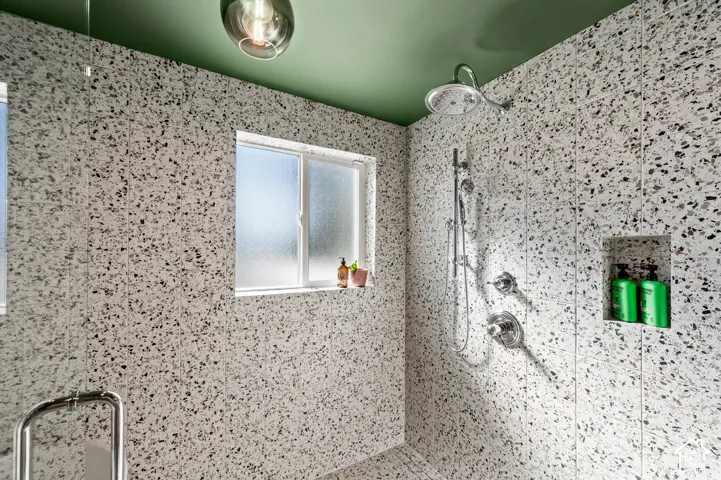 Terrazzo-style tiled shower with a rainfall showerhead, handheld shower fixture, built-in niche, and frosted window