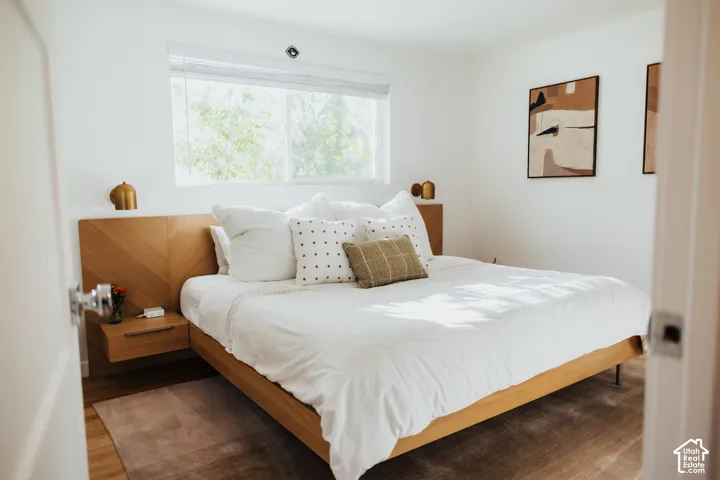 Custom wood-finish headboard featuring an integrated chevron pattern and floating bedside tables, complemented by brass-finish wall-mounted light fixtures and wood-finish flooring