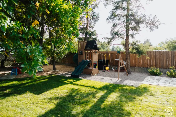 Expansive backyard featuring a manicured lawn, stone patio, mature trees, and wooden perimeter fencing