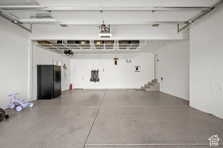 Spacious garage with light grey epoxy flooring, overhead storage racks, and white painted walls