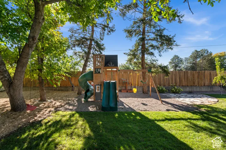 Expansive backyard featuring a manicured lawn, a wooden playset with multiple slides, and a privacy fence