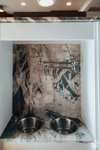 Custom alcove featuring a stone countertop and matching full-height backsplash, polished chrome articulated wall-mounted faucet, and two integrated stainless steel basins