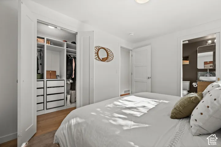 Built-in closet system with shelving and drawers, wood-finish flooring, white doors, and an attached bath with a vessel sink