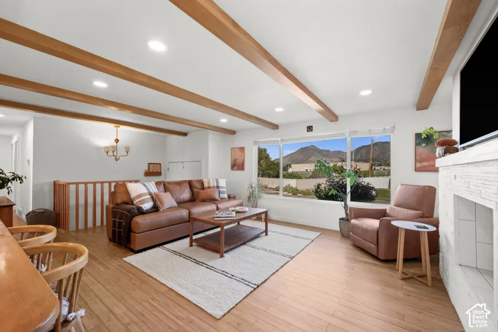 Spacious living area featuring wood-finish flooring, exposed ceiling beams, recessed lighting, and a white stone fireplace