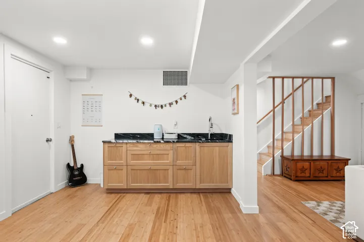 Wood-finish flooring, recessed lighting, built-in cabinetry with dark stone countertop, built-in sink with faucet, and a wood staircase with open risers