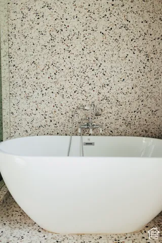 Freestanding white soaking tub with polished chrome deck-mounted faucet and handheld shower sprayer, set against full-height terrazzo wall and floor tiling