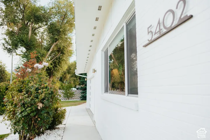 White brick exterior featuring a concrete walkway, recessed soffit lighting, and metal house numerals