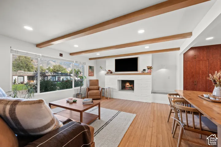 Hardwood flooring, painted brick fireplace, recessed lighting, wood ceiling beams, and expansive windows