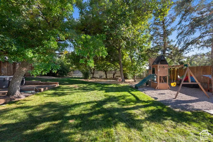 Expansive backyard featuring a manicured lawn, mature trees, wood fencing, and a built-in wood deck