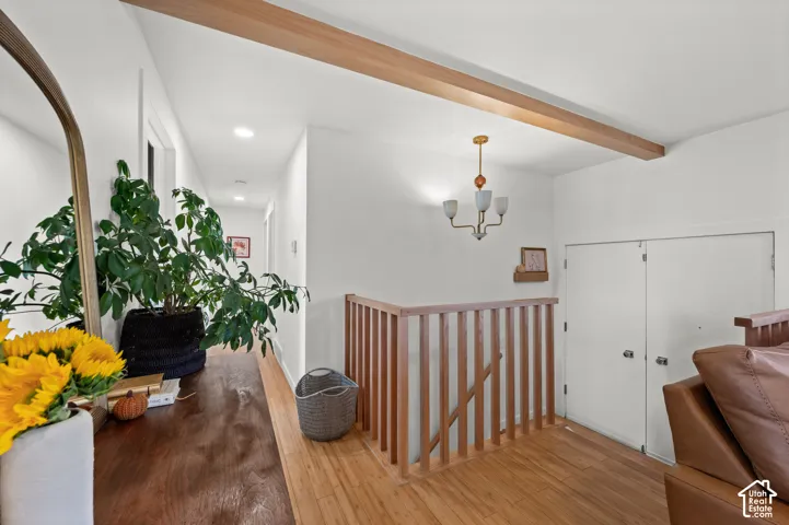 Hardwood flooring, painted white walls, wood beam ceiling accent, wood stair railing, and a modern chandelier