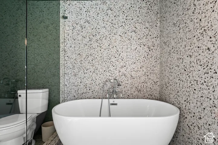 Freestanding soaking tub with a floor-mounted faucet, complemented by speckled wall tiling and a glass shower enclosure