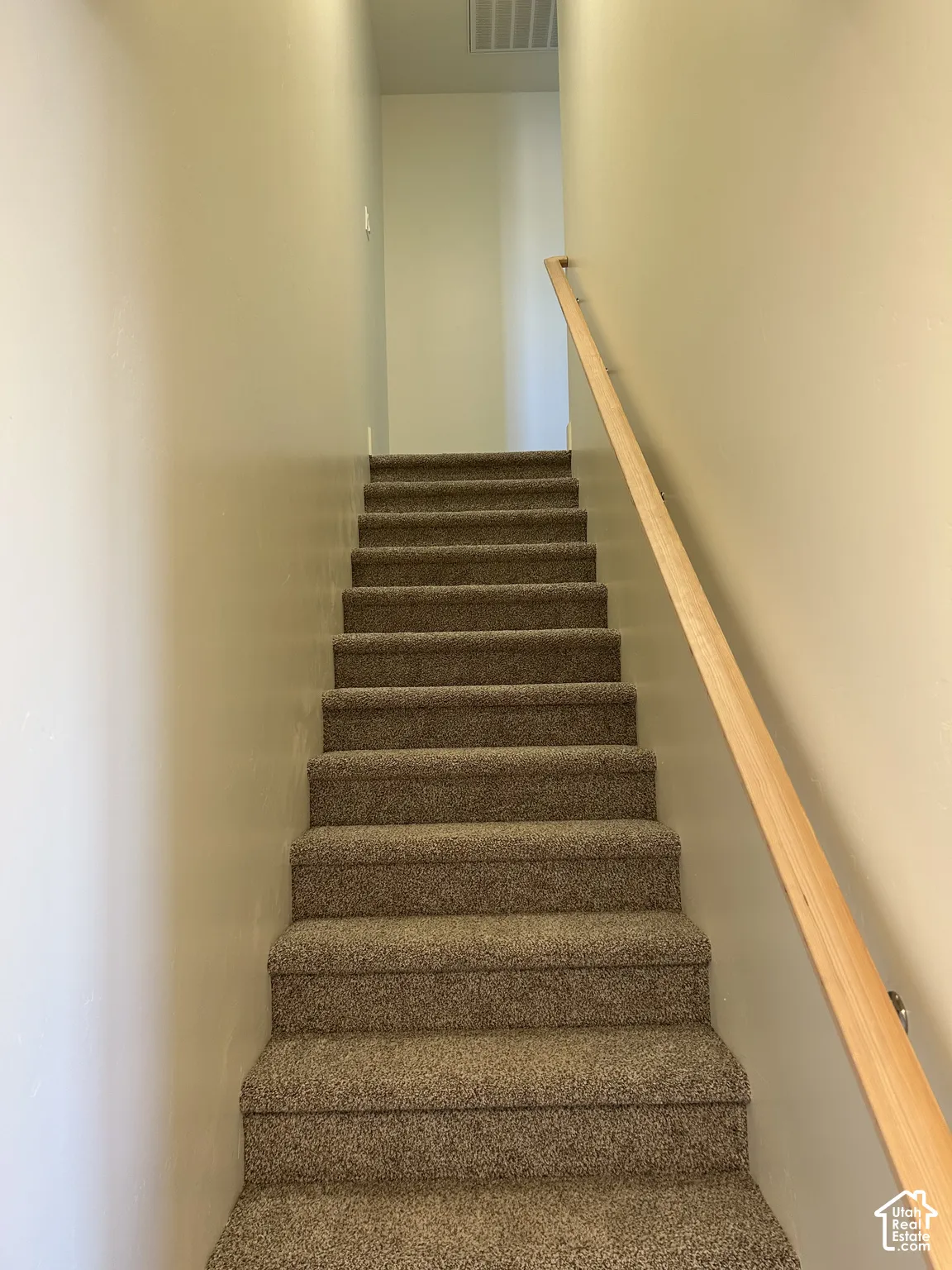 Carpeted staircase featuring a light wood handrail and neutral wall finishes