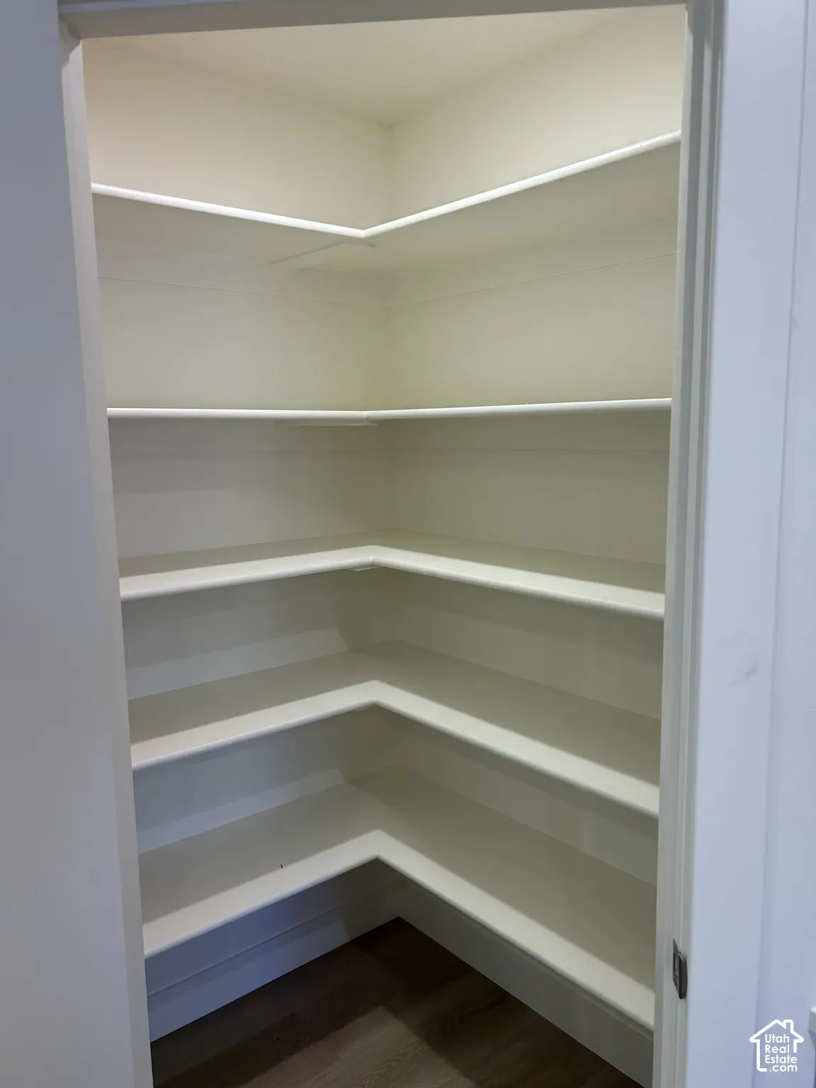 Corner pantry with multiple white shelves and wood-finish flooring
