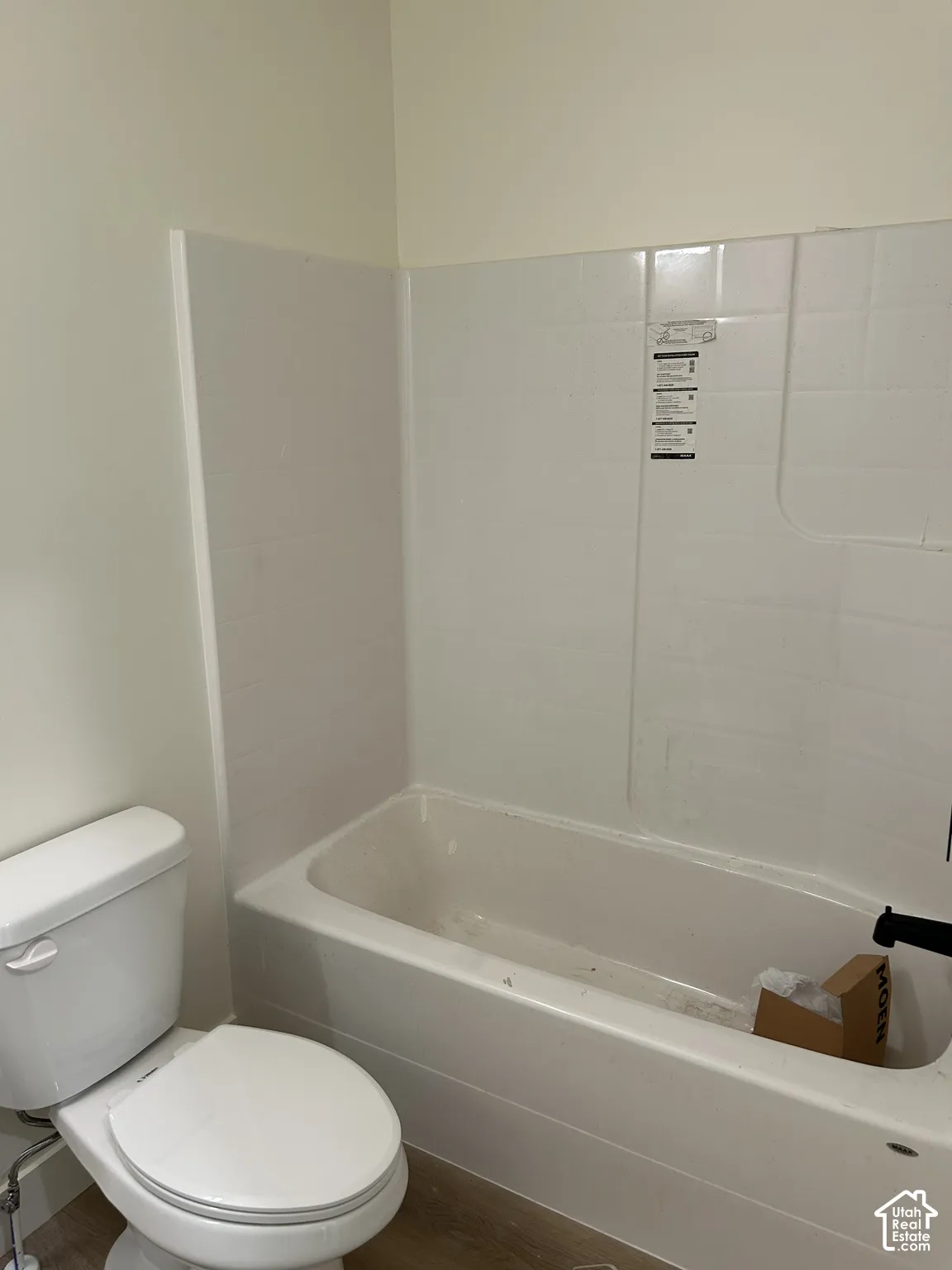 White tub and shower combination with white tile surround, adjacent to a white toilet with a closed lid