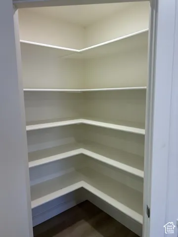 Corner pantry with multiple white shelves and wood-finish flooring