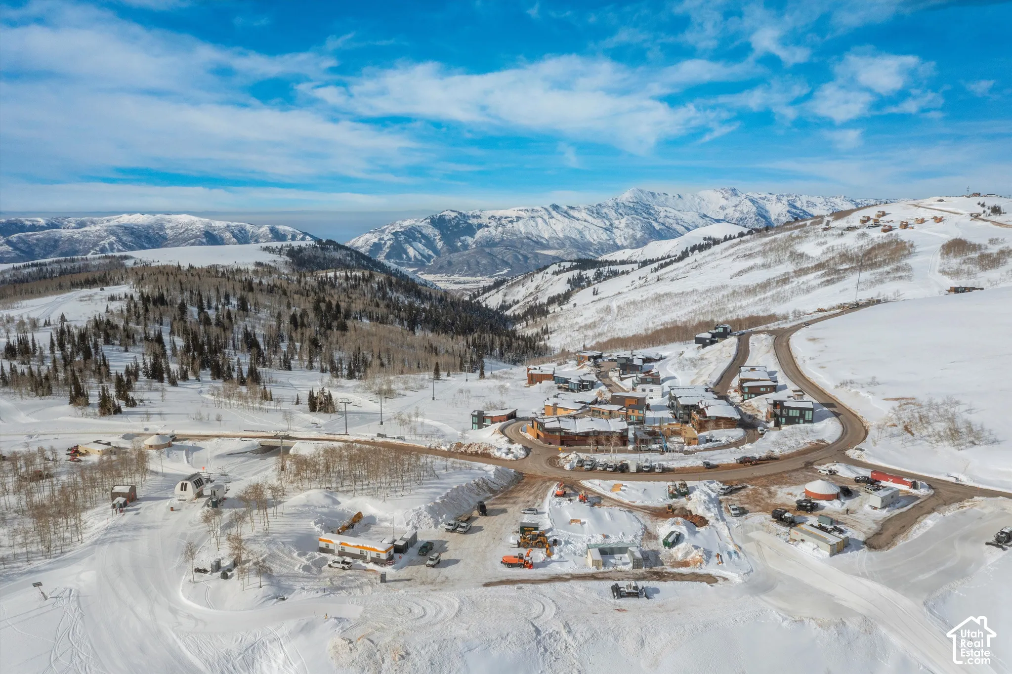 Snow-covered mountainous landscape featuring dispersed residences, a winding road network, and extensive evergreen tree coverage