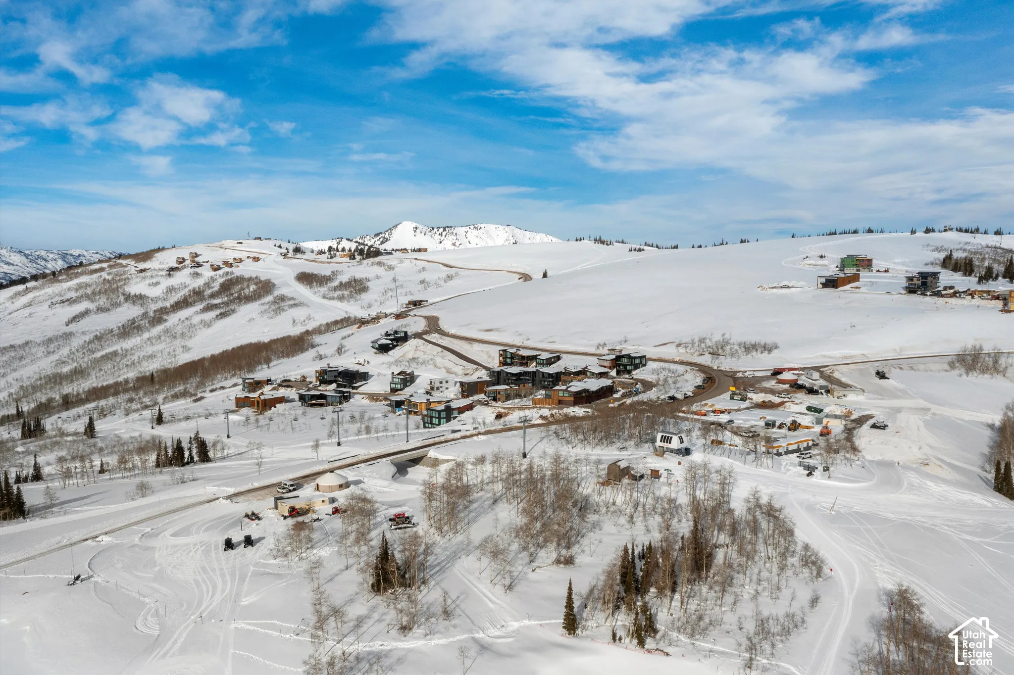 Snow-covered mountain landscape with multiple residential structures, winding roads, and scattered deciduous trees