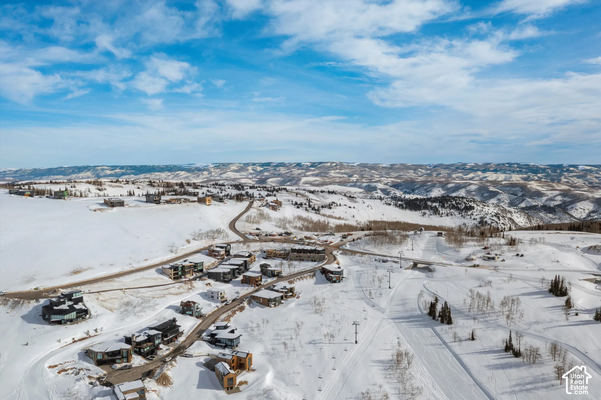 Expansive snow-covered landscape with scattered residential properties, winding roads, and distant mountain ranges