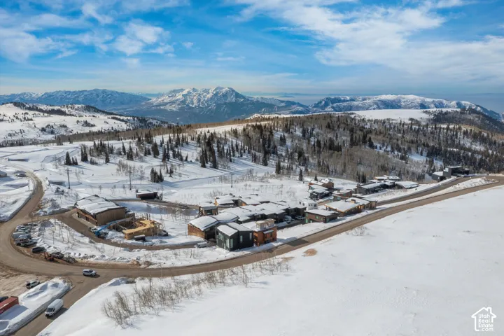 Snow-covered landscape featuring a development of contemporary residences, mountain terrain, and a winding paved road