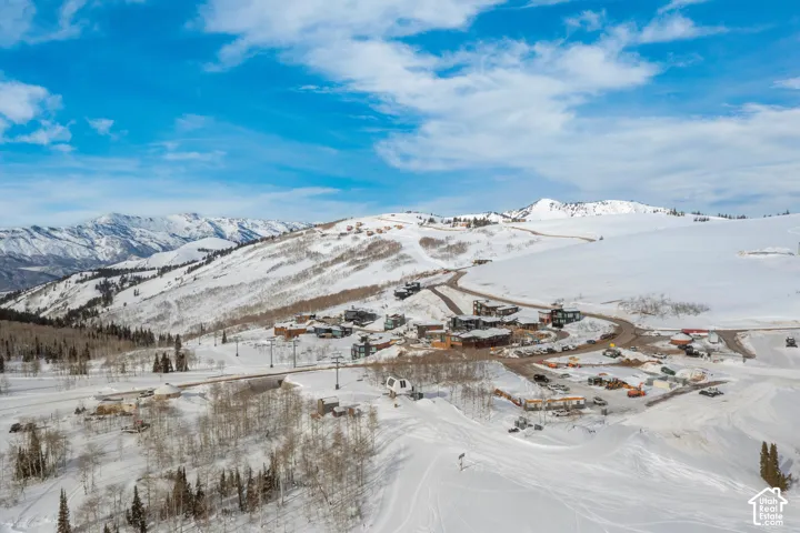 Snow-covered mountain landscape with multiple structures, paved roads, and exposed ski lifts
