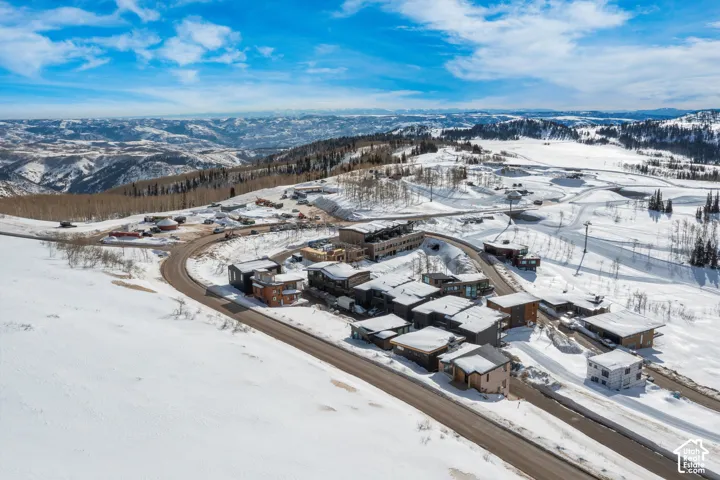Snow-covered mountainous terrain featuring a cluster of properties with varied architectural styles, paved roadways, and scattered evergreen trees