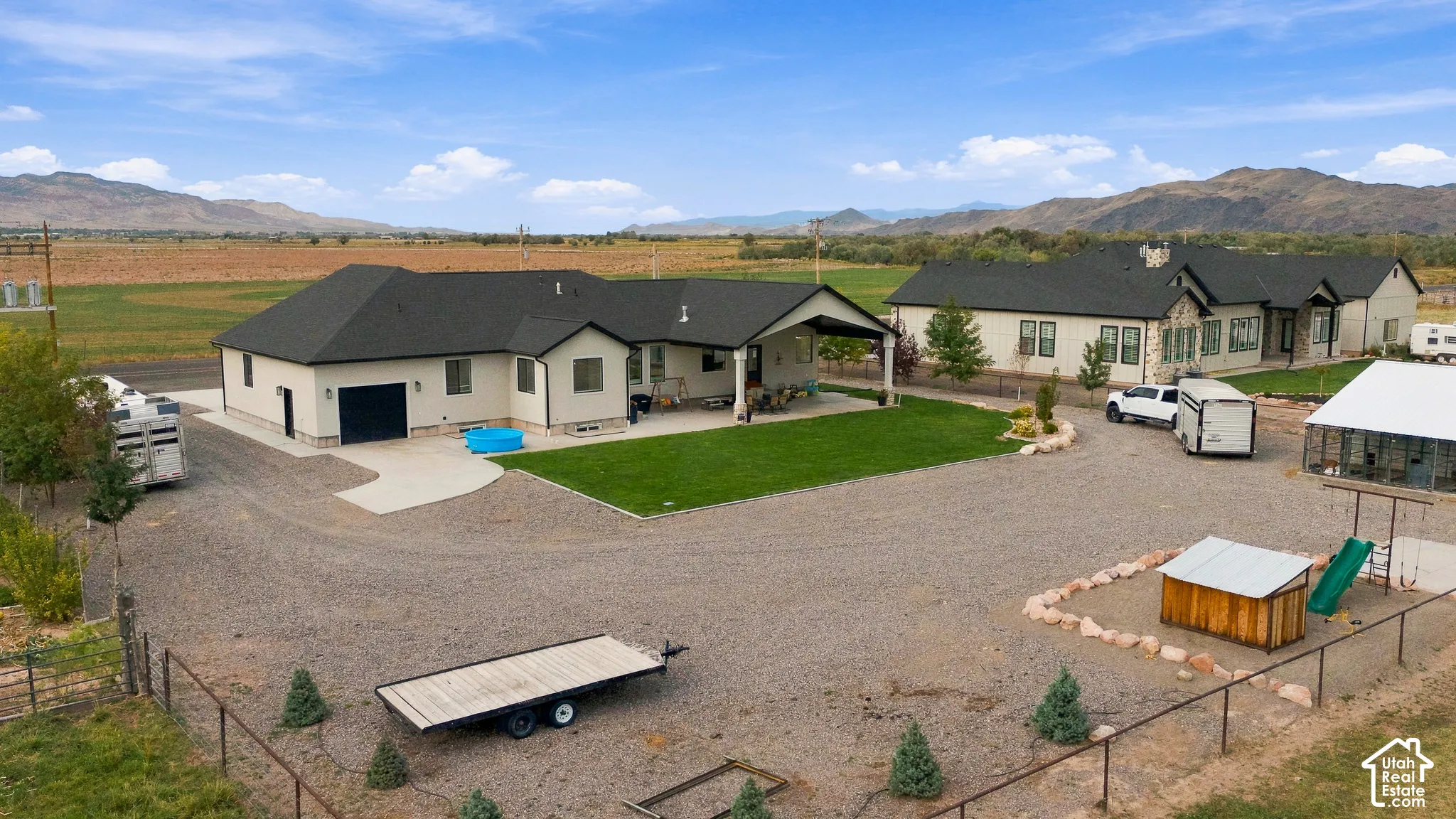 Expansive gravel driveway, manicured lawn, covered patio, dark shingle roofs, and distant mountain scenery