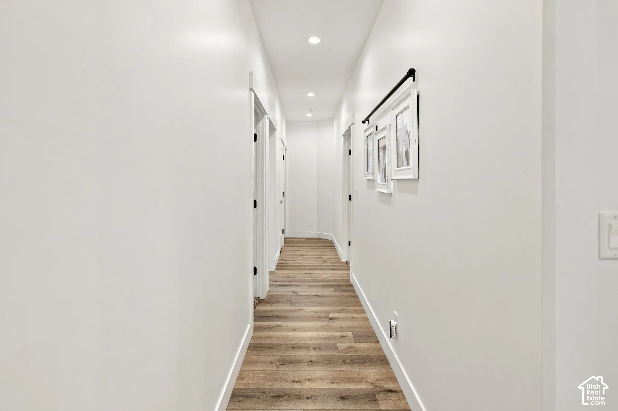 Hallway featuring wood-finish flooring, recessed lighting, and multiple doorways with dark hardware