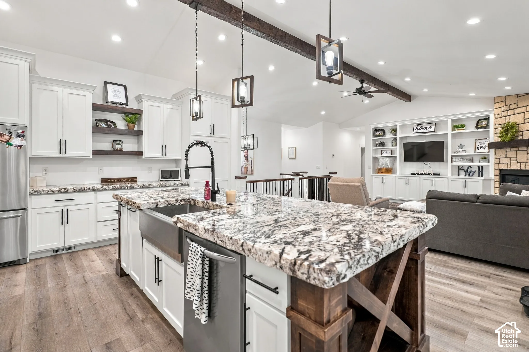 Chef's kitchen featuring white cabinetry with black hardware, a large center island with a decorative wood base and speckled stone countertop with undermount sink, stainless steel appliances, pendant lighting, recessed ceiling lights, and wood-finish floo