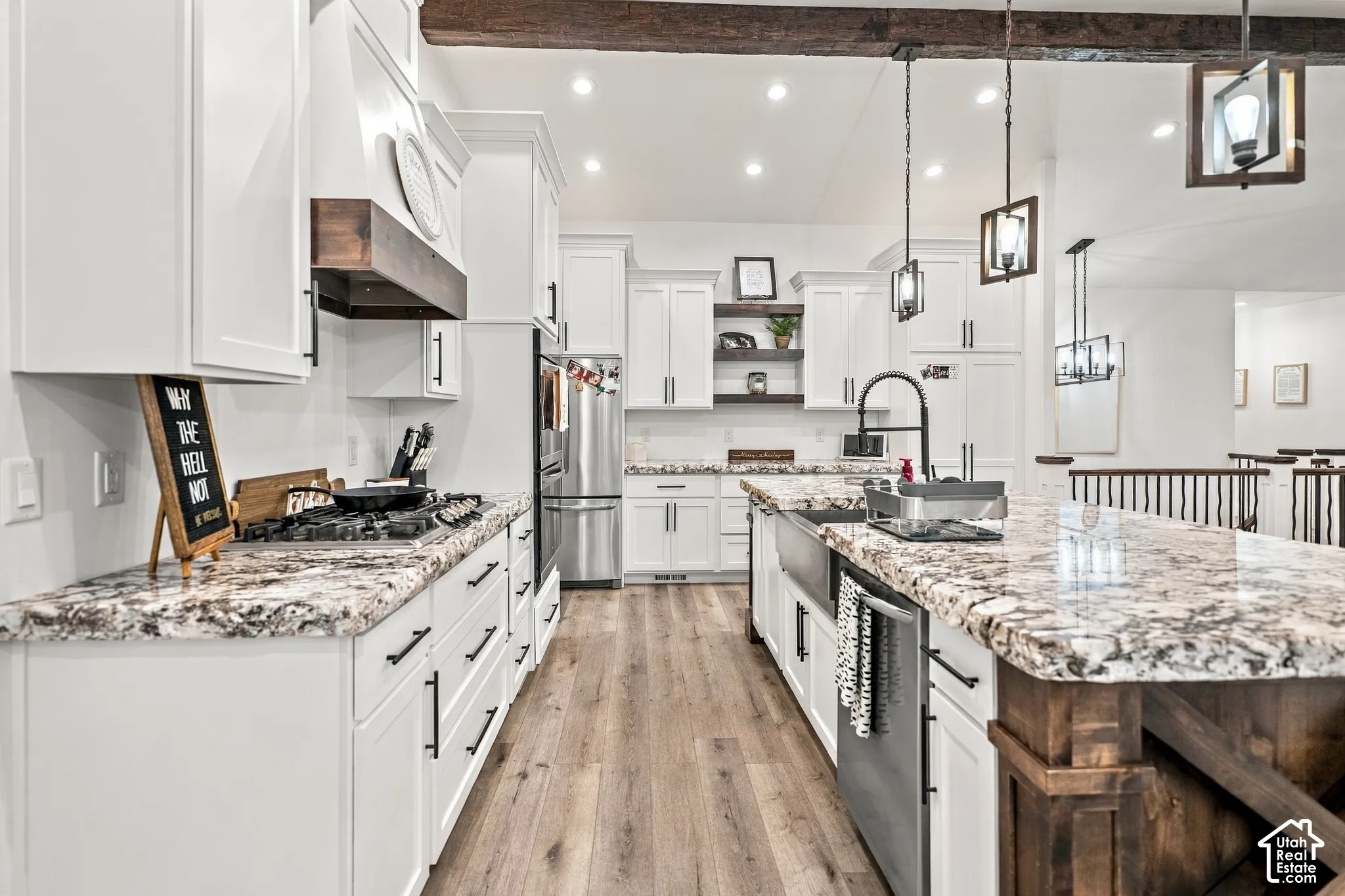 Spacious kitchen featuring white cabinetry, wood-finish flooring, a kitchen island with a farmhouse sink, stainless steel appliances, and pendant lighting