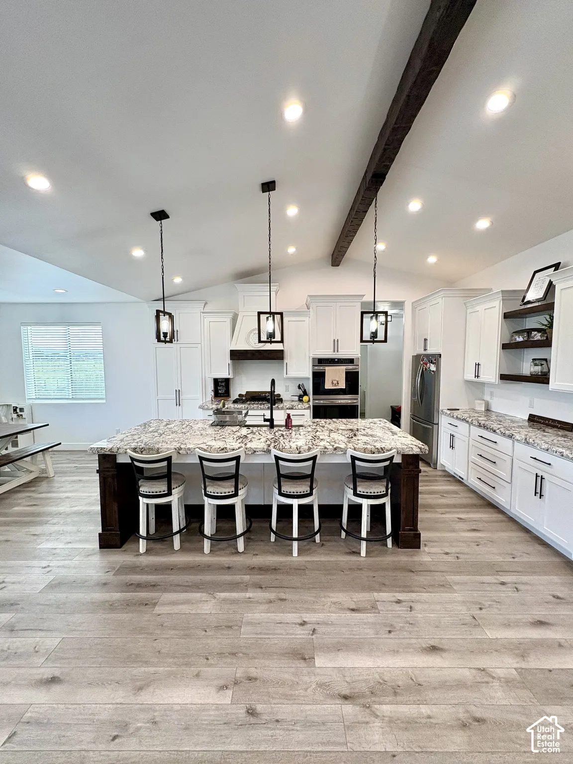 Kitchen featuring a large island with stone countertop, white cabinetry with dark hardware, wood-finish flooring, recessed lighting, and exposed ceiling beam