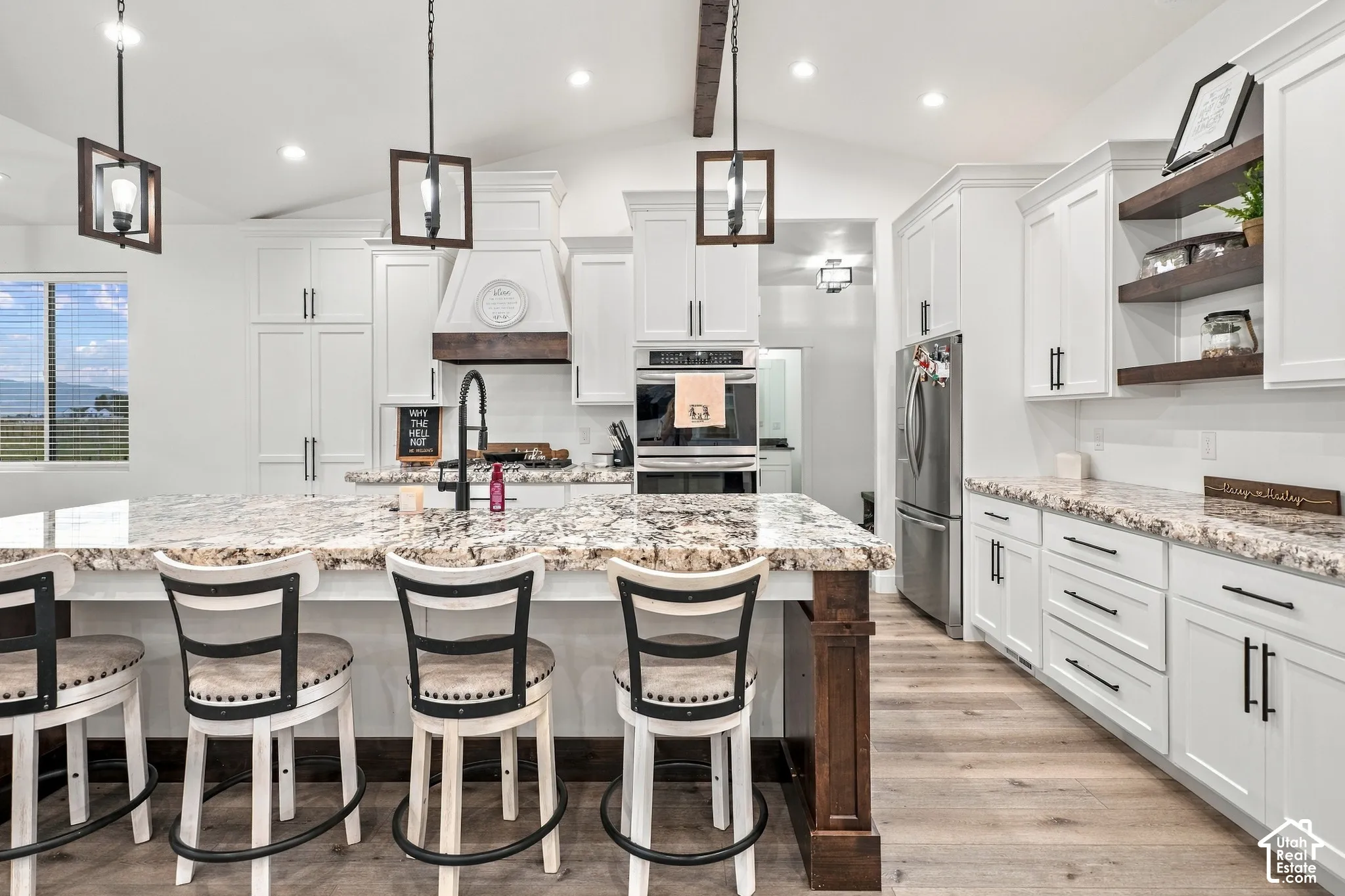 Spacious kitchen featuring an expansive center island with seating, white cabinetry, built-in stainless steel appliances, and wood-finish flooring