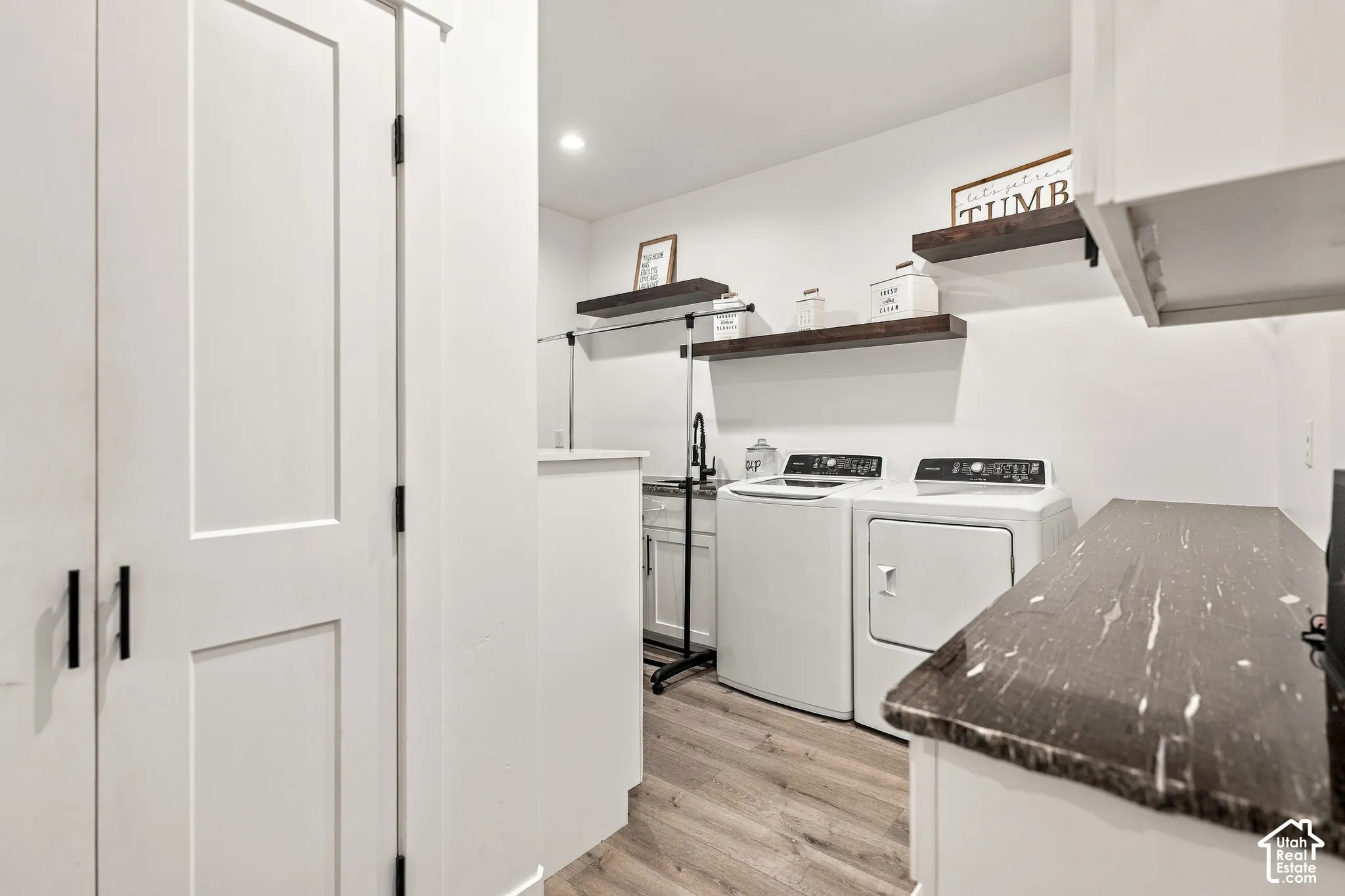 White shaker cabinetry with modern black pulls, wood-finish flooring, dark stone-finish countertop, white walls, and recessed lighting