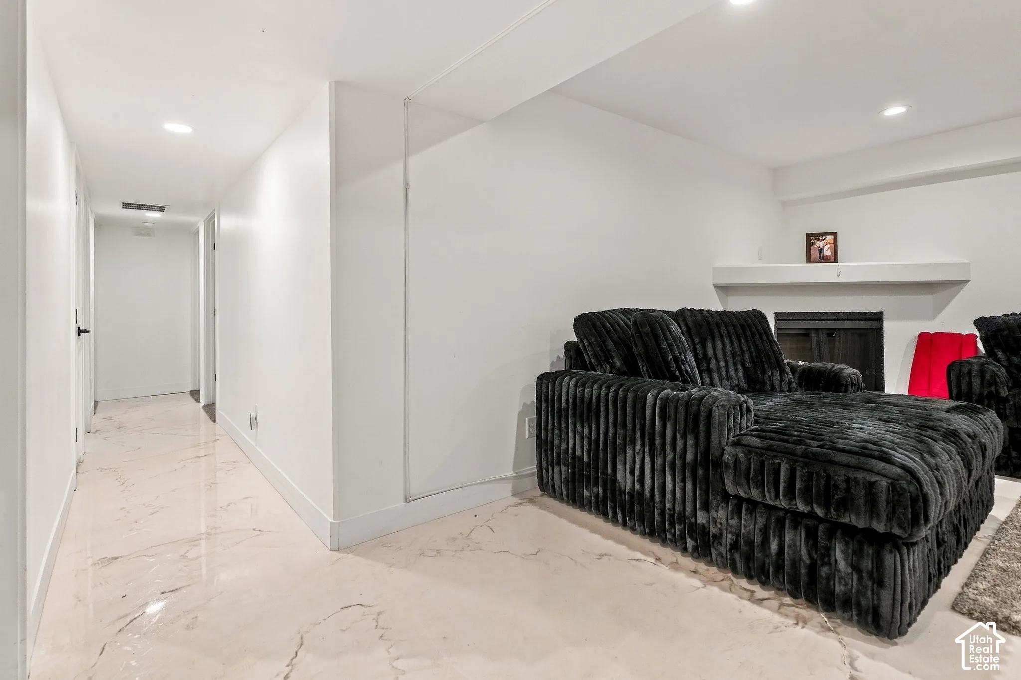Recessed lighting, polished stone-look flooring, white painted walls, and a fireplace with a white mantel