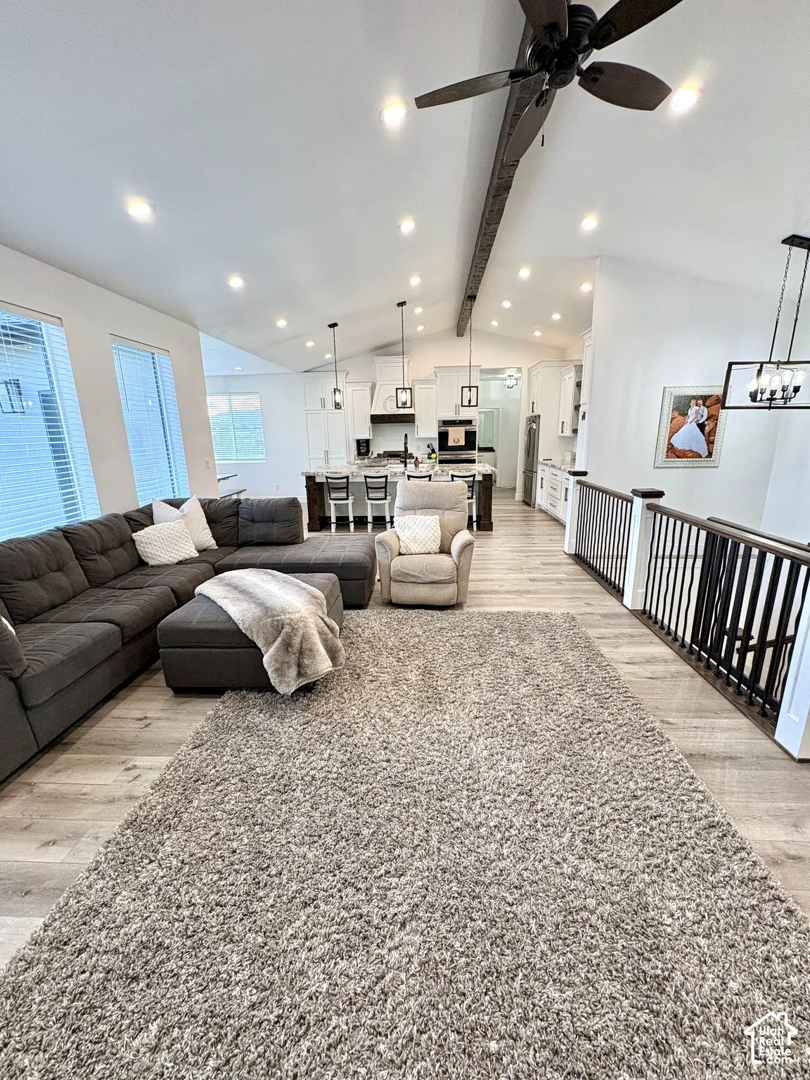 Vaulted ceiling with exposed beam, recessed lighting, wood-finish flooring, white kitchen cabinetry, and dark kitchen island with pendant lighting