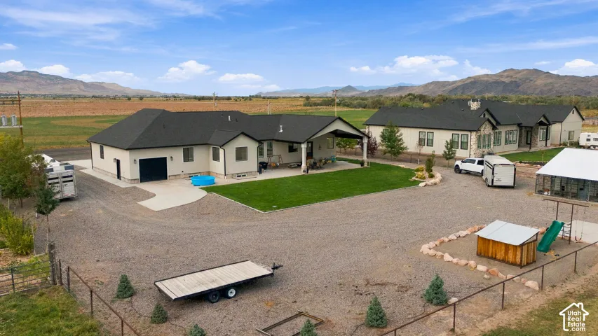 Expansive gravel driveway, manicured lawn, covered patio, dark shingle roofs, and distant mountain scenery
